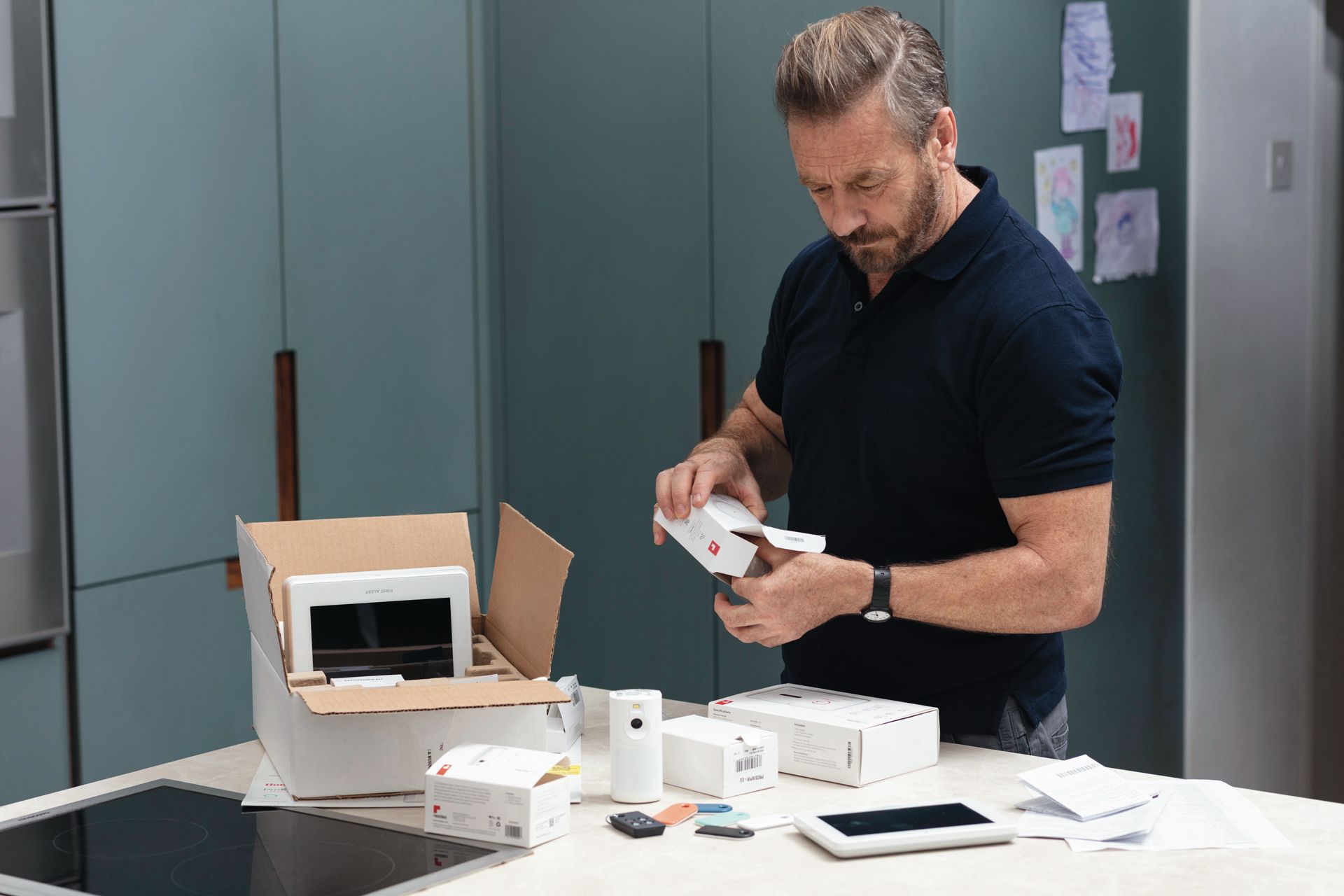 Man in black shirt unpacking a small white device at a table in a kitchen-like room