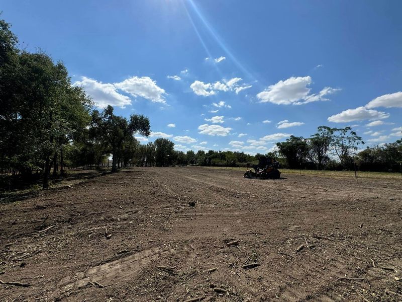 A large, cleared plot of dirt under a bright blue sky with scattered trees in the distance and a small tractor nearby.