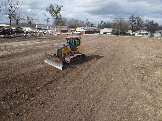 A yellow bulldozer leveling a large, cleared field under a cloudy sky.