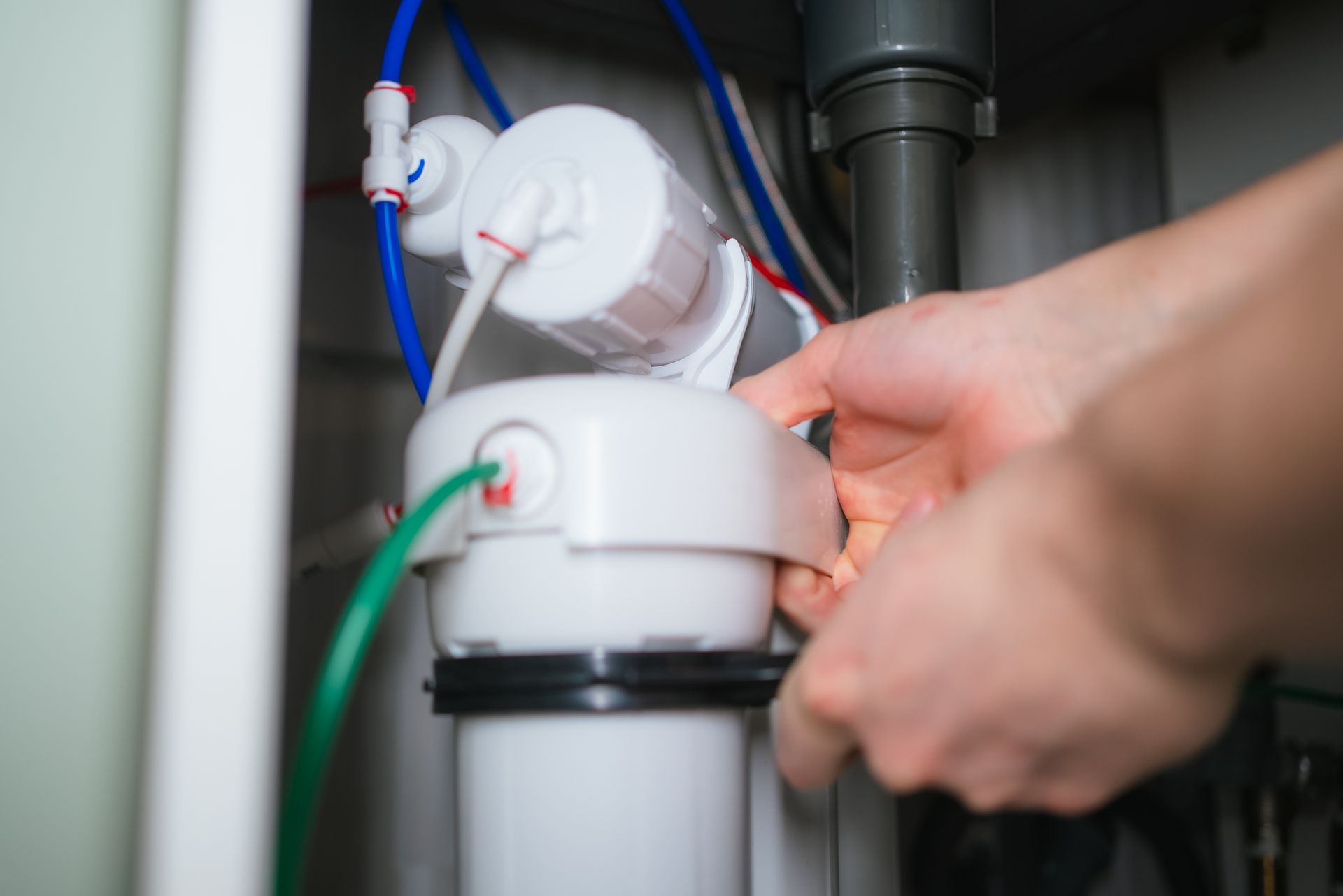 Hands replacing a cartridge on an under-sink water filtration system with colored tubing