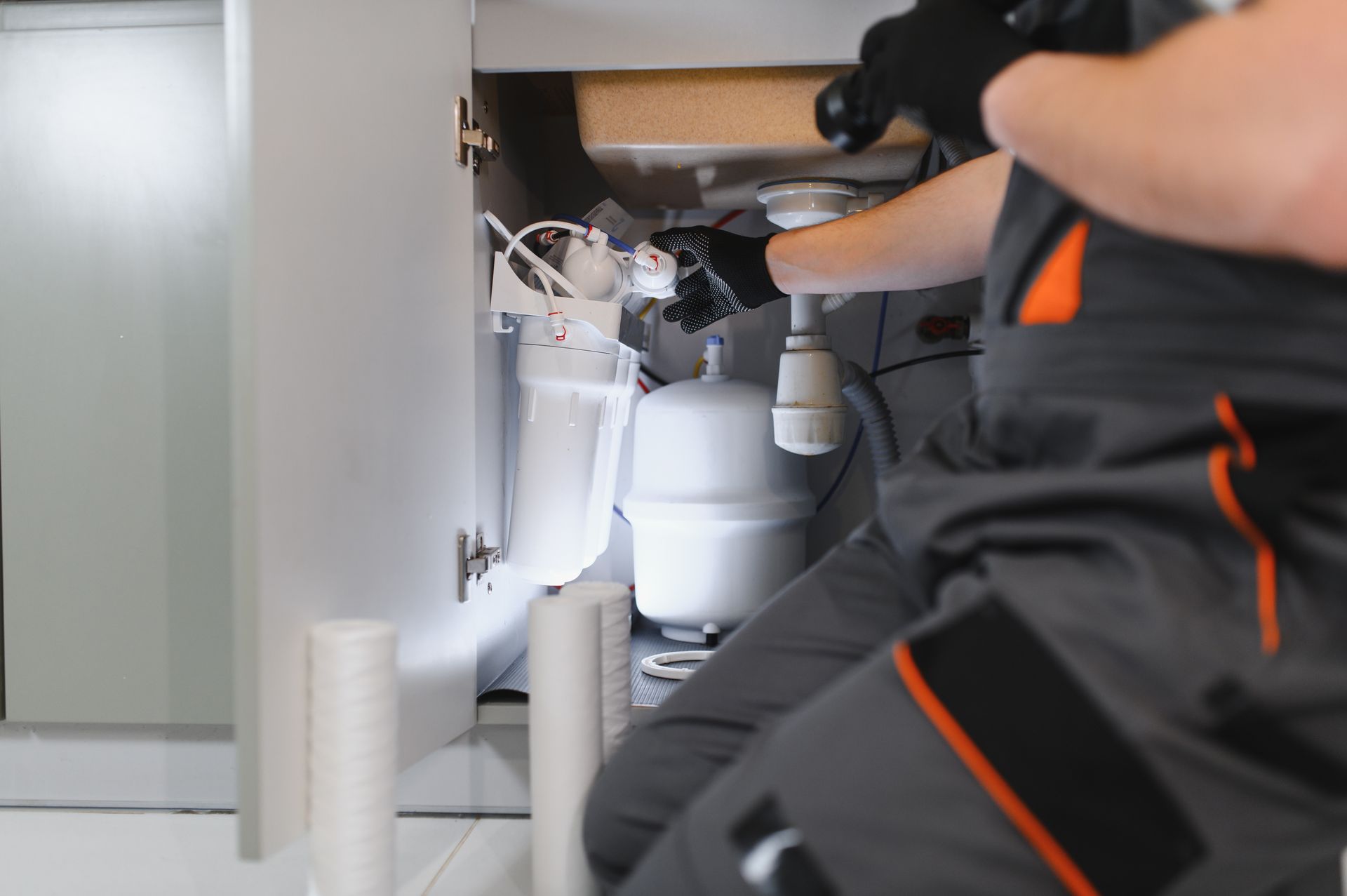 A plumber replacing white sediment filter cartridges in an under-sink water filtration system A plumber replacing white sediment filter cartridges in an under-sink water filtration system