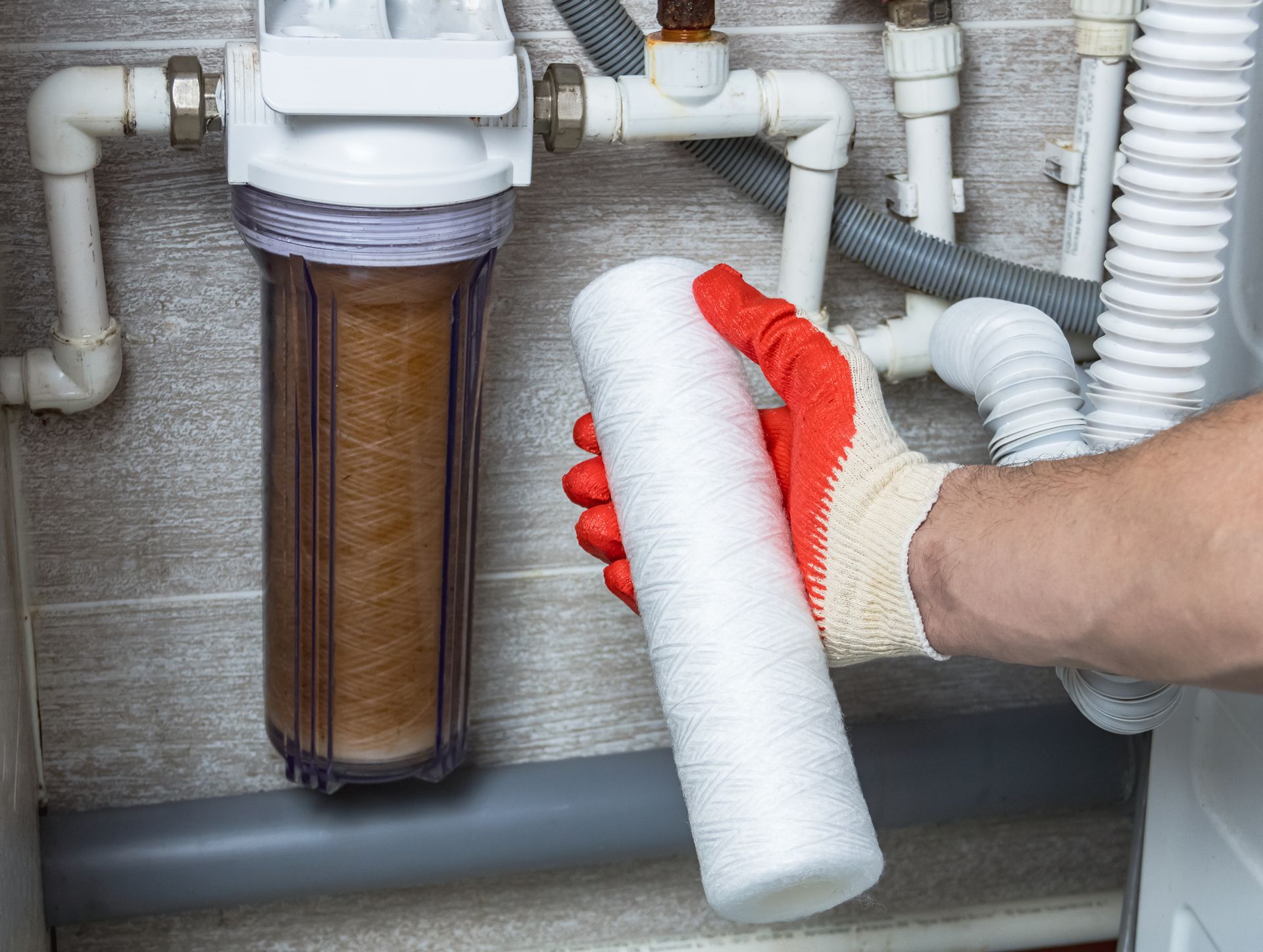 Men's hands replace a dirty water filter cartridge with a new clean one under the sink.
