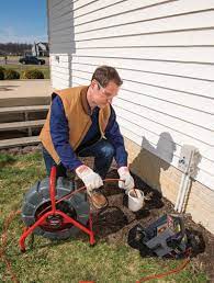 Man using plumbing inspection equipment next to a house; outdoors on grass.