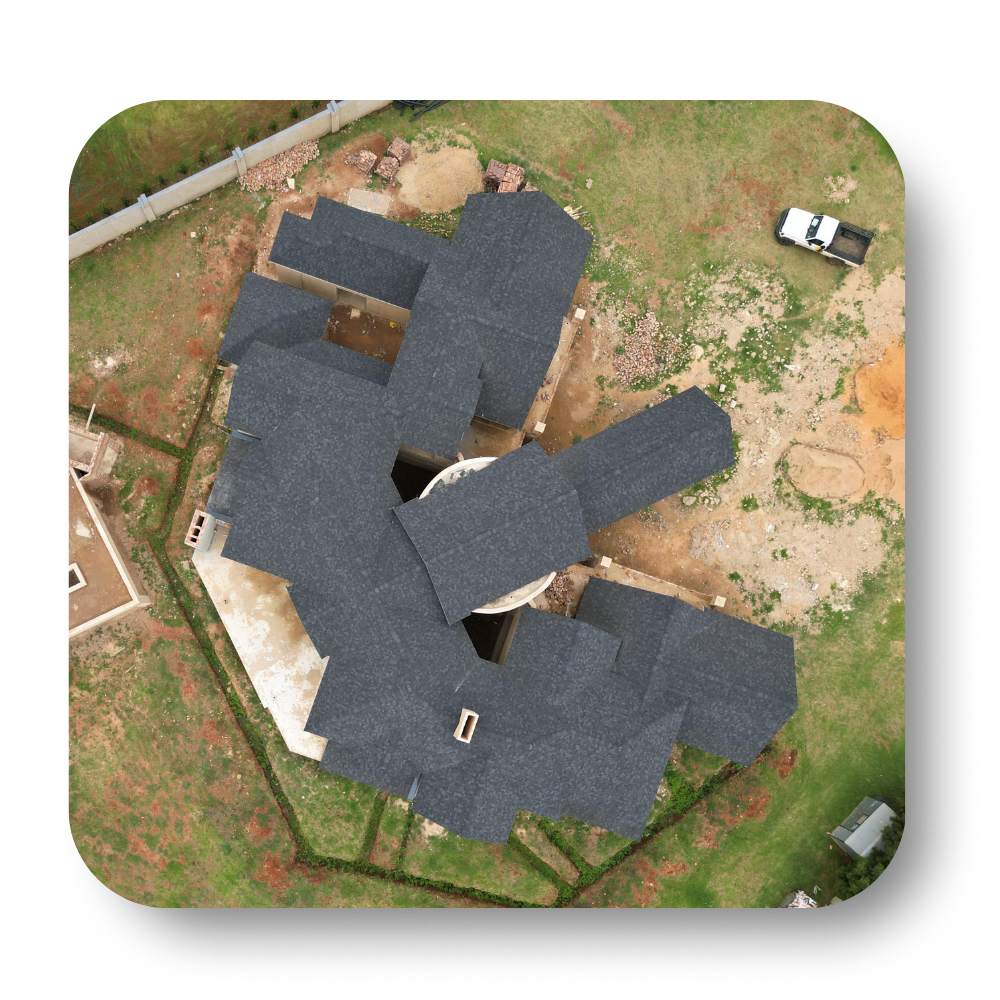 Aerial view of a house with dark roof and small yard, surrounded by dirt and fencing.
