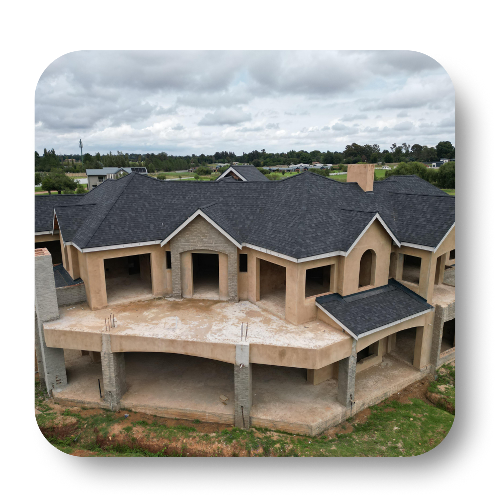 Large unfinished two-story house with dark roof and beige walls on a concrete frame under cloudy sky