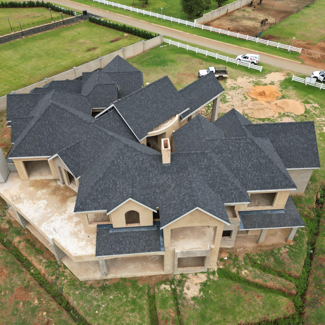 Aerial view of a large unfinished tan house with dark gray roof in a grassy lot.