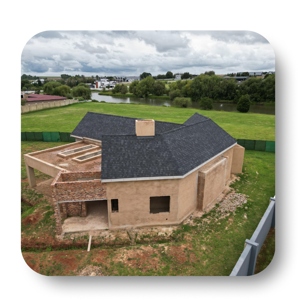 Partially built house with dark roof and brick walls in a grassy field under cloudy skies