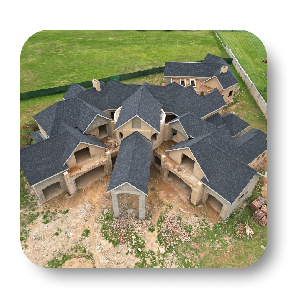 Aerial view of a large unfinished house with dark roofs and tan walls on a grassy lot.