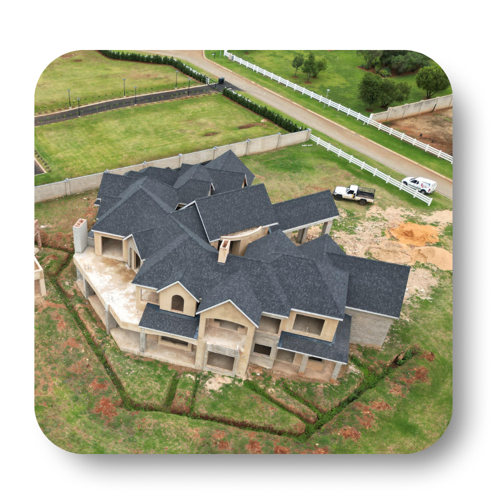 Aerial view of a large unfinished house with a dark roof, surrounded by grass and a driveway.