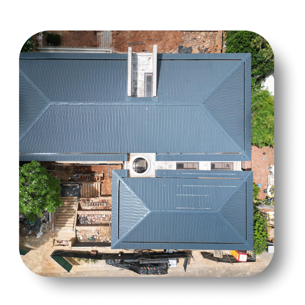 Aerial view of a house with a blue metal roof and surrounding trees and driveway
