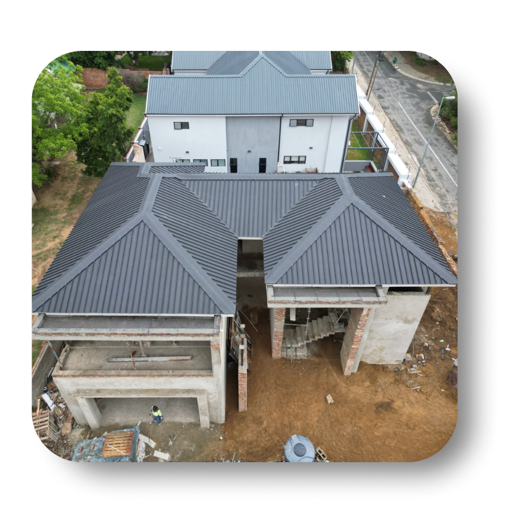 Aerial view of a house with a dark gray roof and unfinished concrete structure beside it.