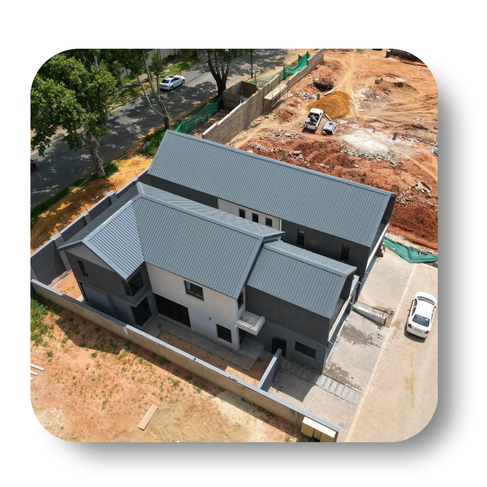 Aerial view of a gray-roofed house under construction beside a dirt lot and roadway.