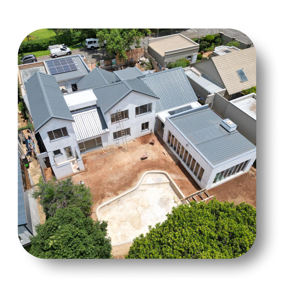 Aerial view of a large white house with gray roofs, a bare yard, and a concrete pool area.