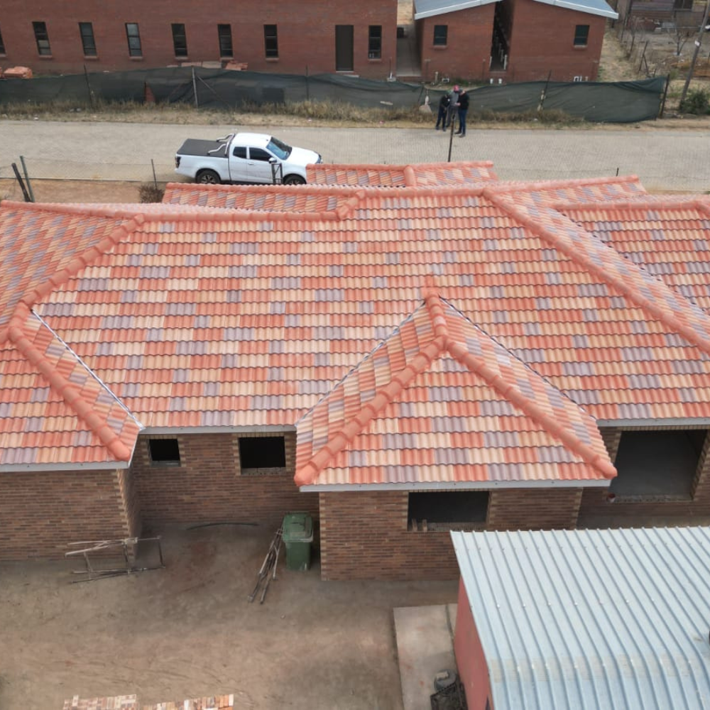 Aerial view of red-tiled brick buildings, a white pickup truck, and two people near a dirt road.