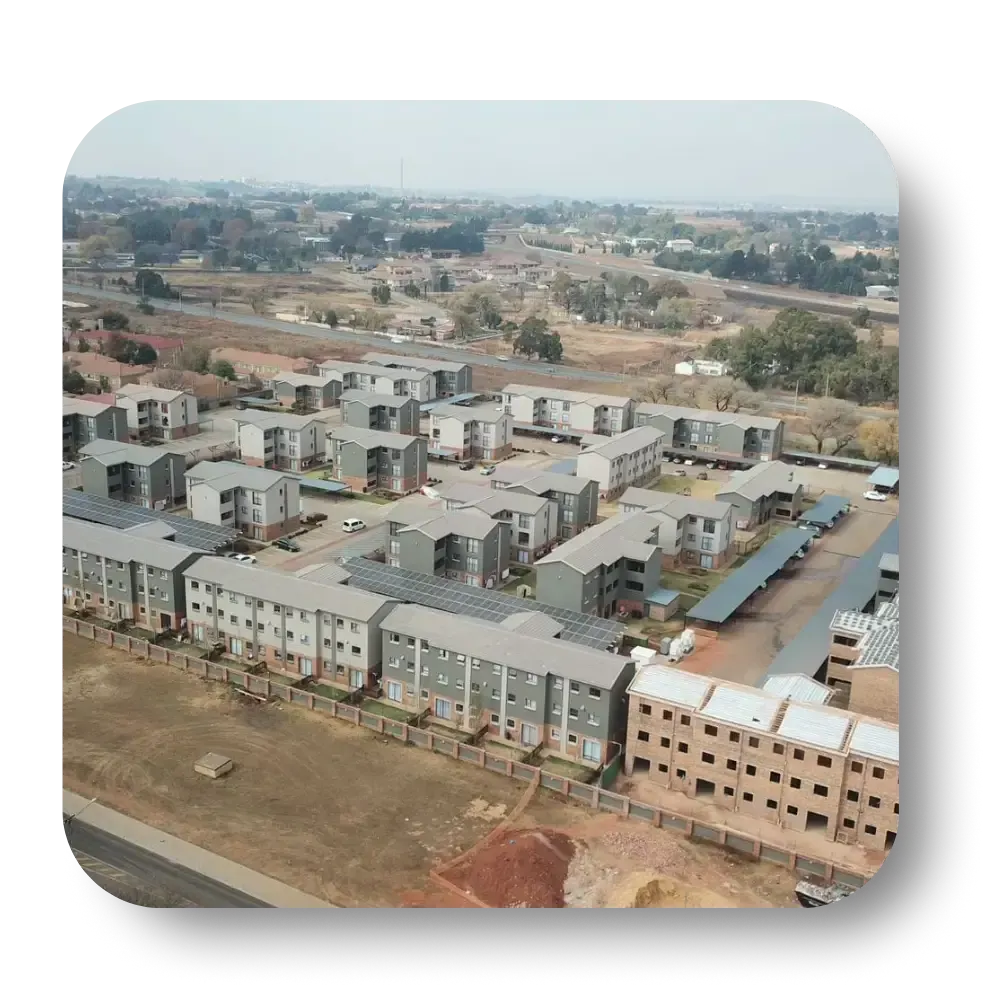 Aerial view of a residential complex with rows of low-rise buildings and open land beyond.