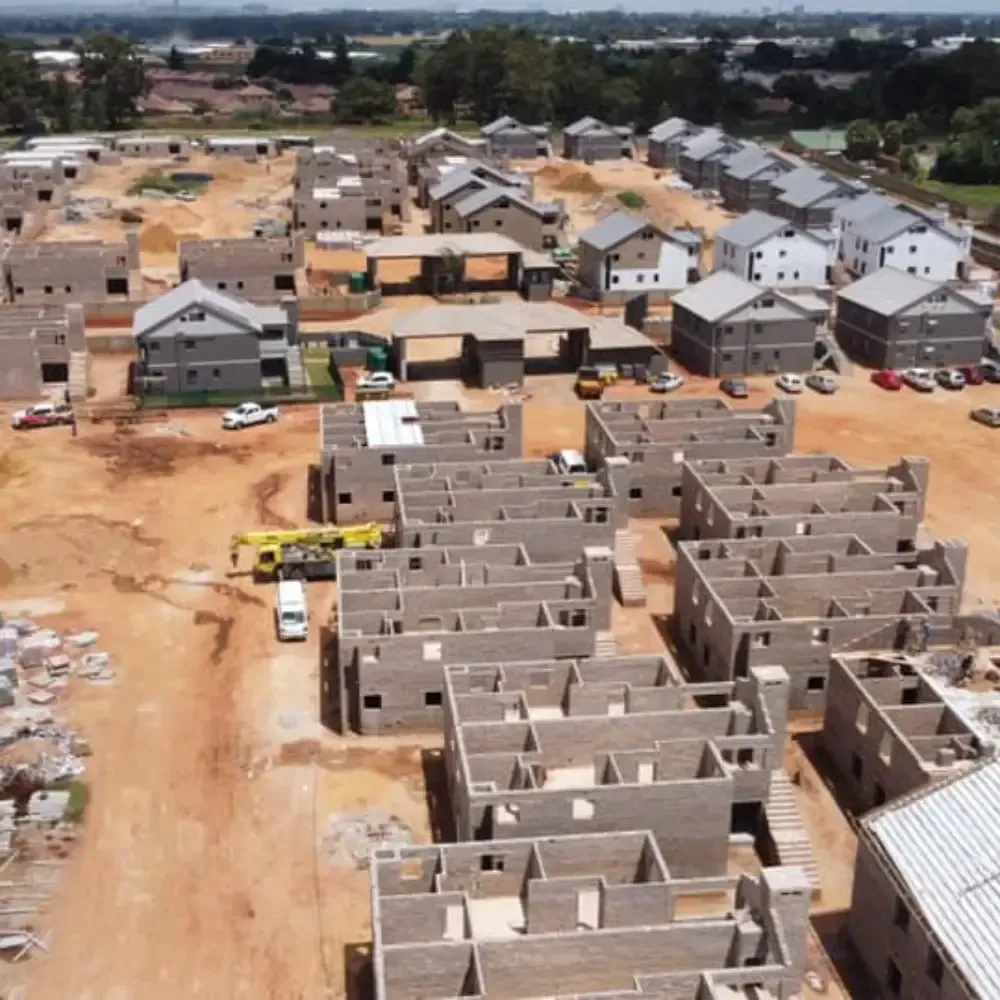 Aerial view of a housing development under construction with rows of unfinished concrete homes and dirt roads.