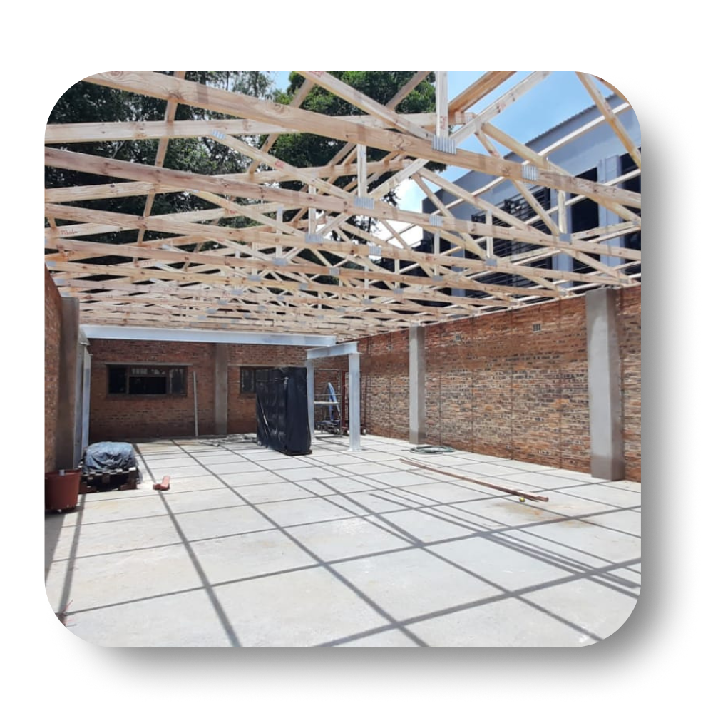 Partially built brick room with exposed roof trusses and concrete floor in bright sunlight