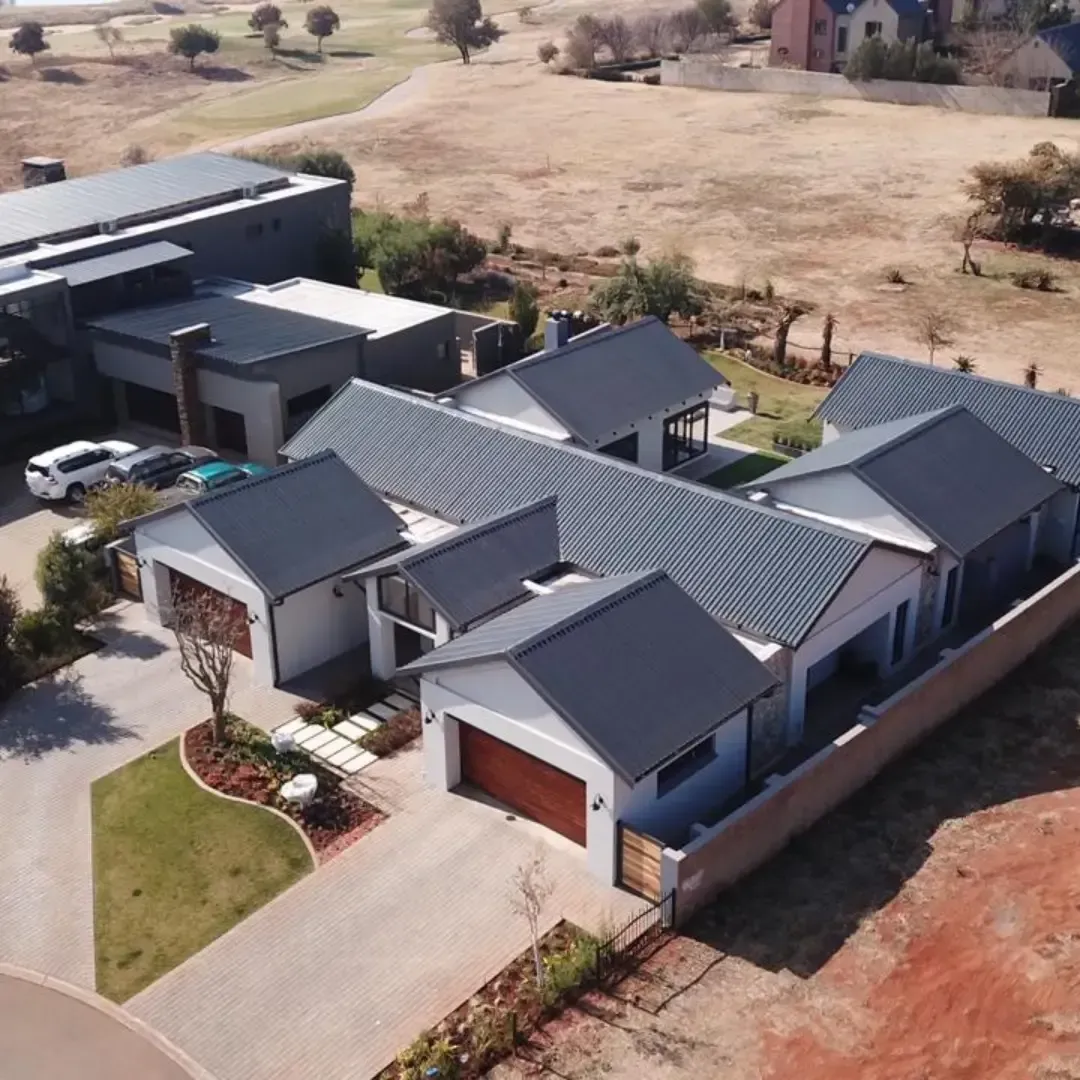 Aerial view of a brick house under construction with a dark blue roof in a suburban neighborhood.