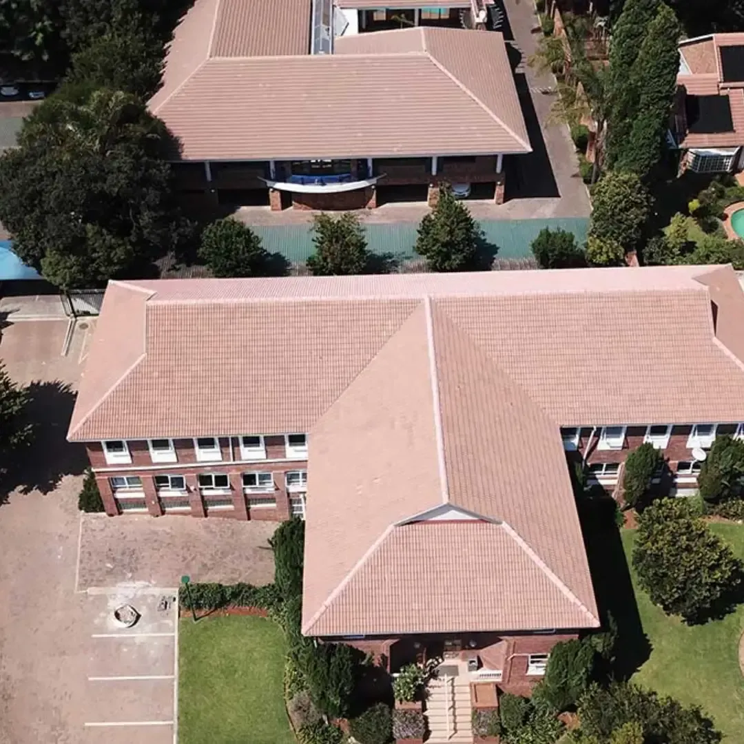 Aerial view of a tan-roofed campus building with surrounding trees and lawns.