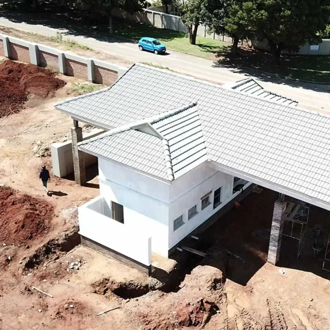 Aerial view of a white house under construction with a tiled roof and dirt around it.
