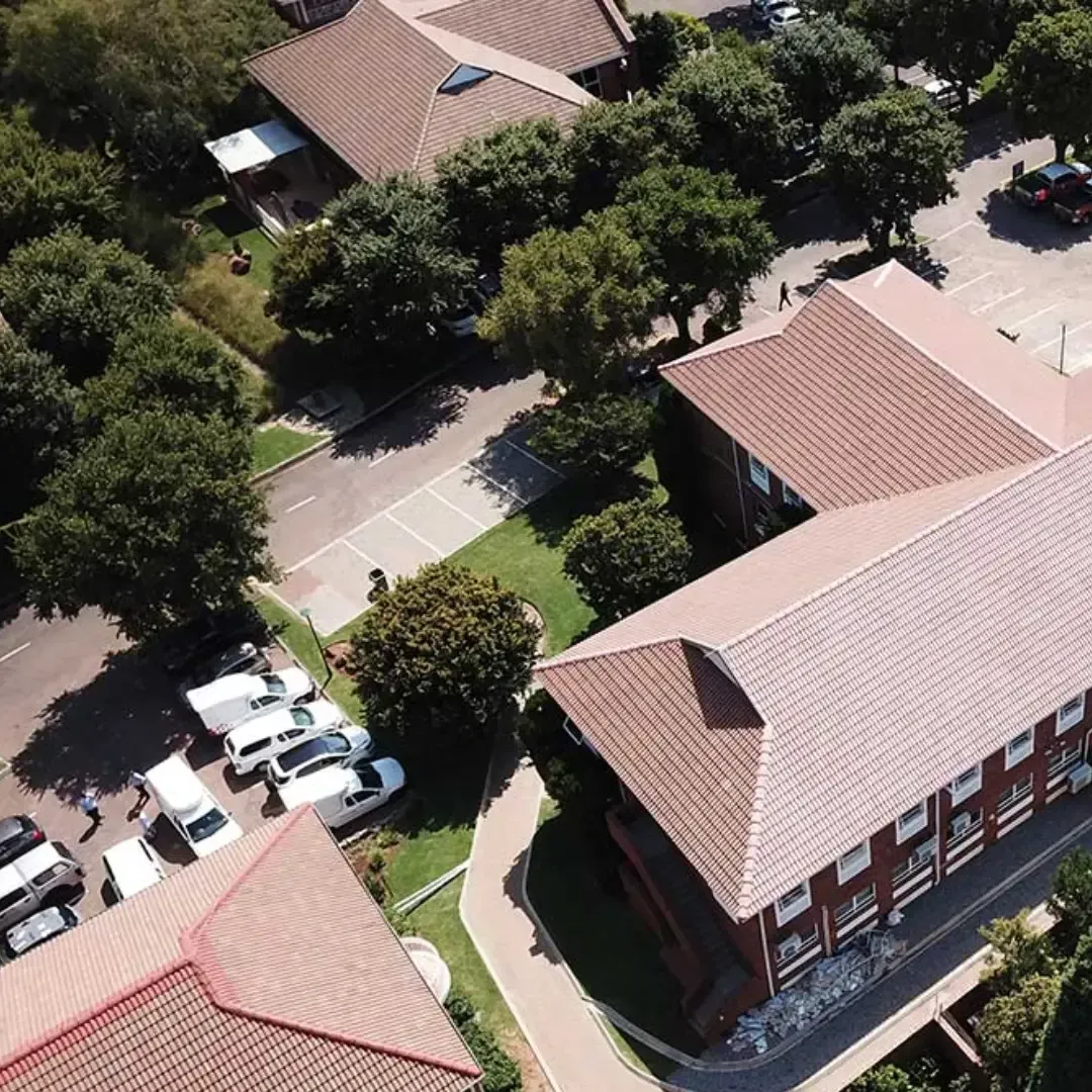 Aerial view of a red-roofed building, trees, parked cars, and a curved walkway on a campus-like area