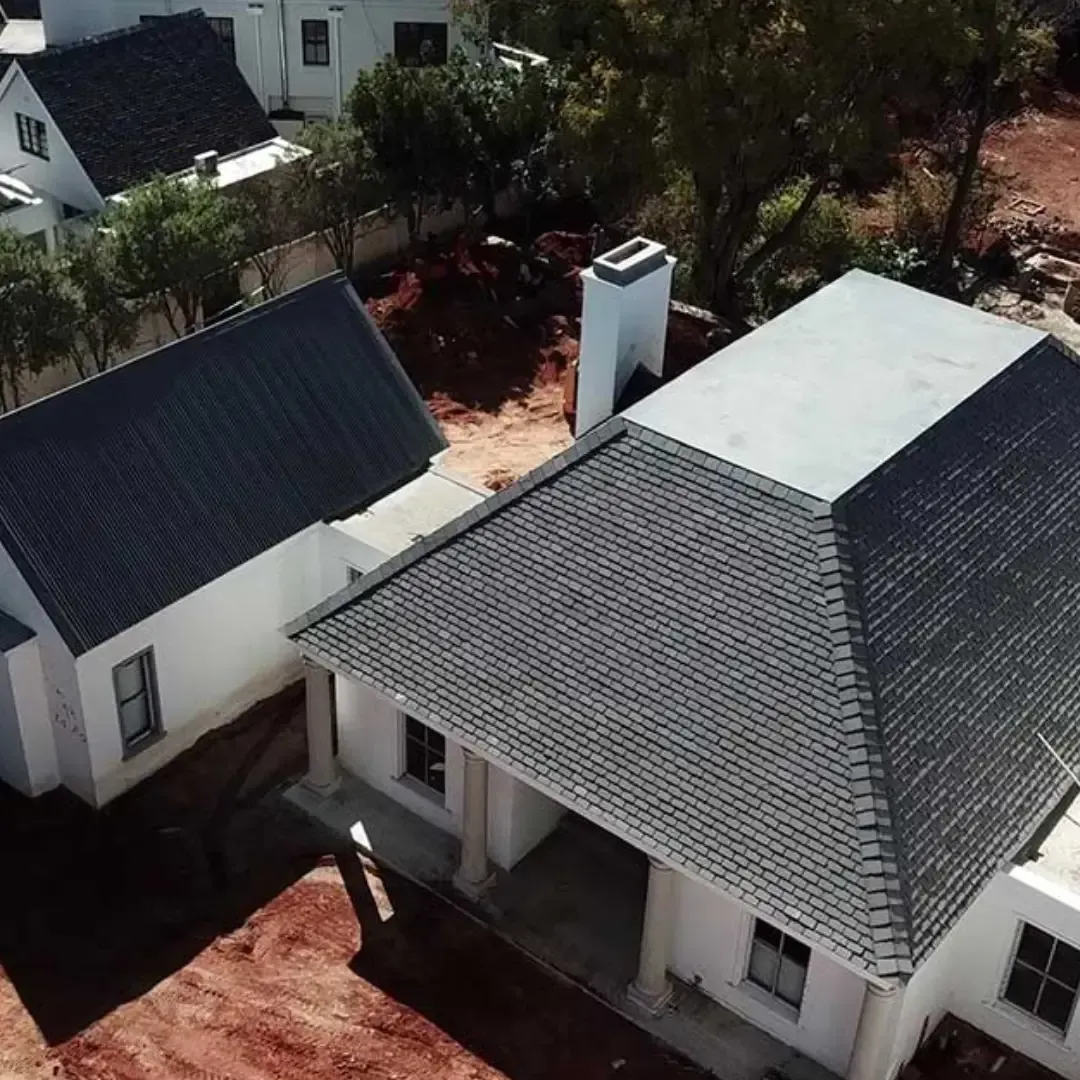 Aerial view of two white houses with dark roofs and a porch, surrounded by trees and red dirt.