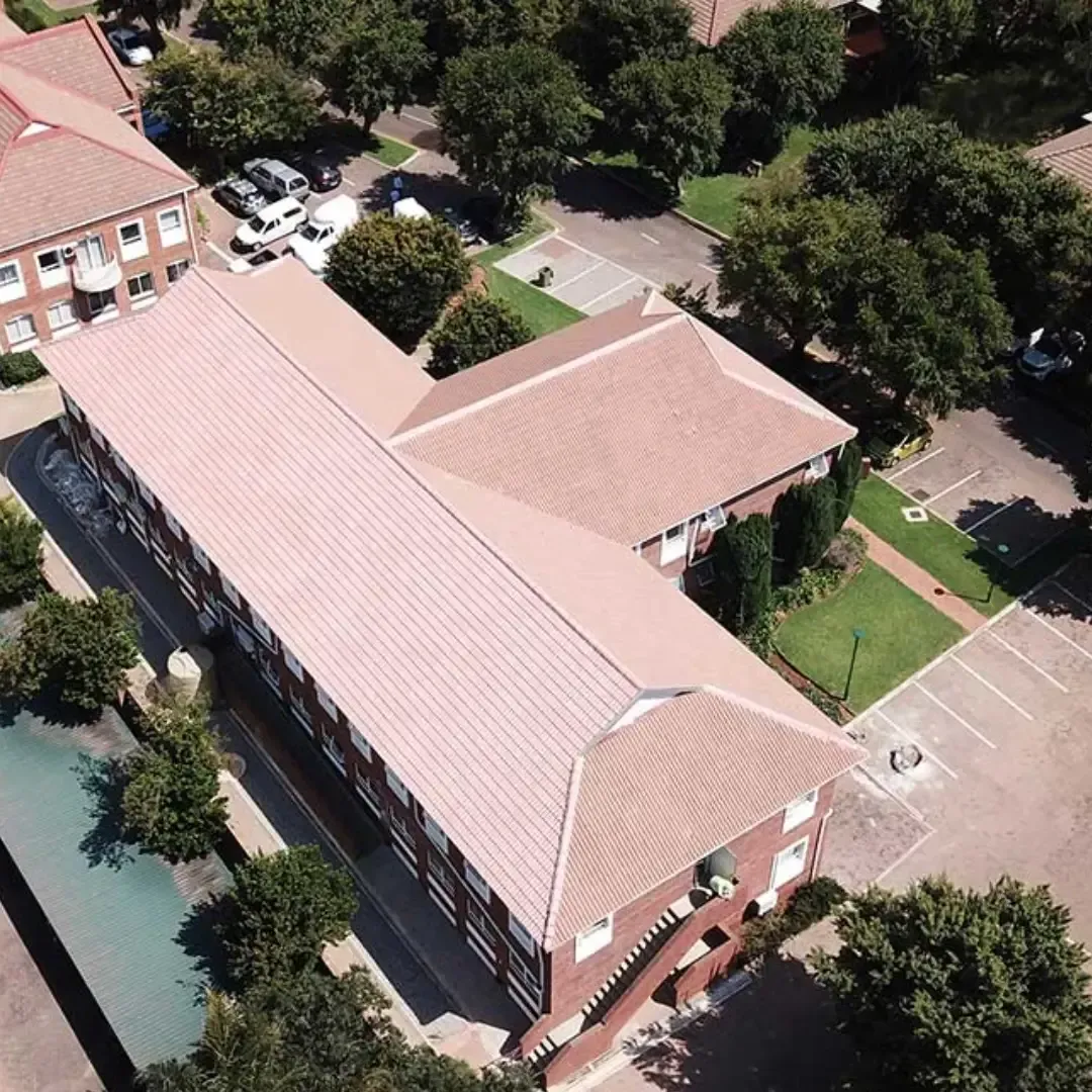 Aerial view of a red-roofed brick building surrounded by trees and a paved courtyard.