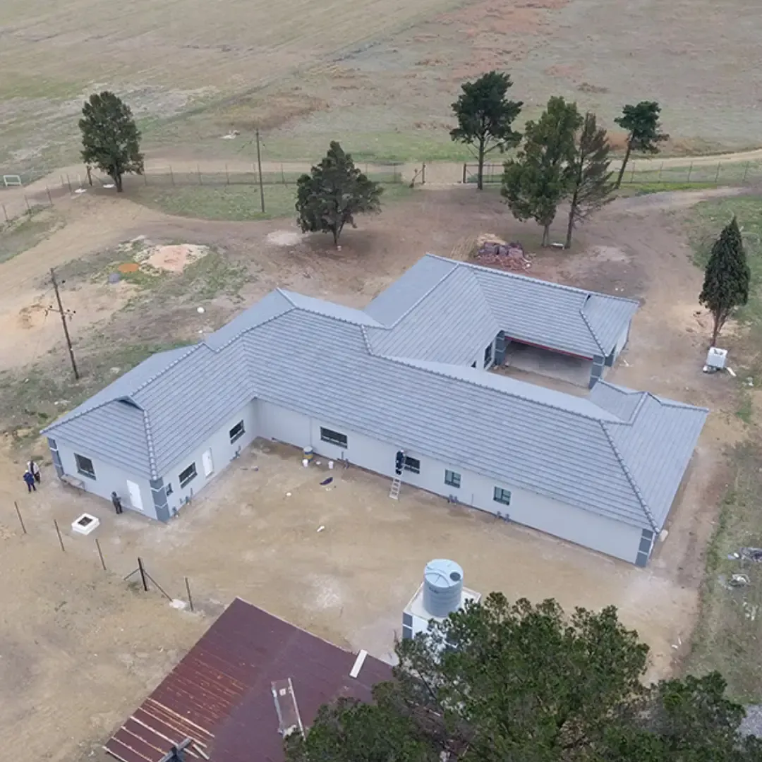 Aerial view of a gray-roofed rural house with yard, trees, and nearby outbuildings.