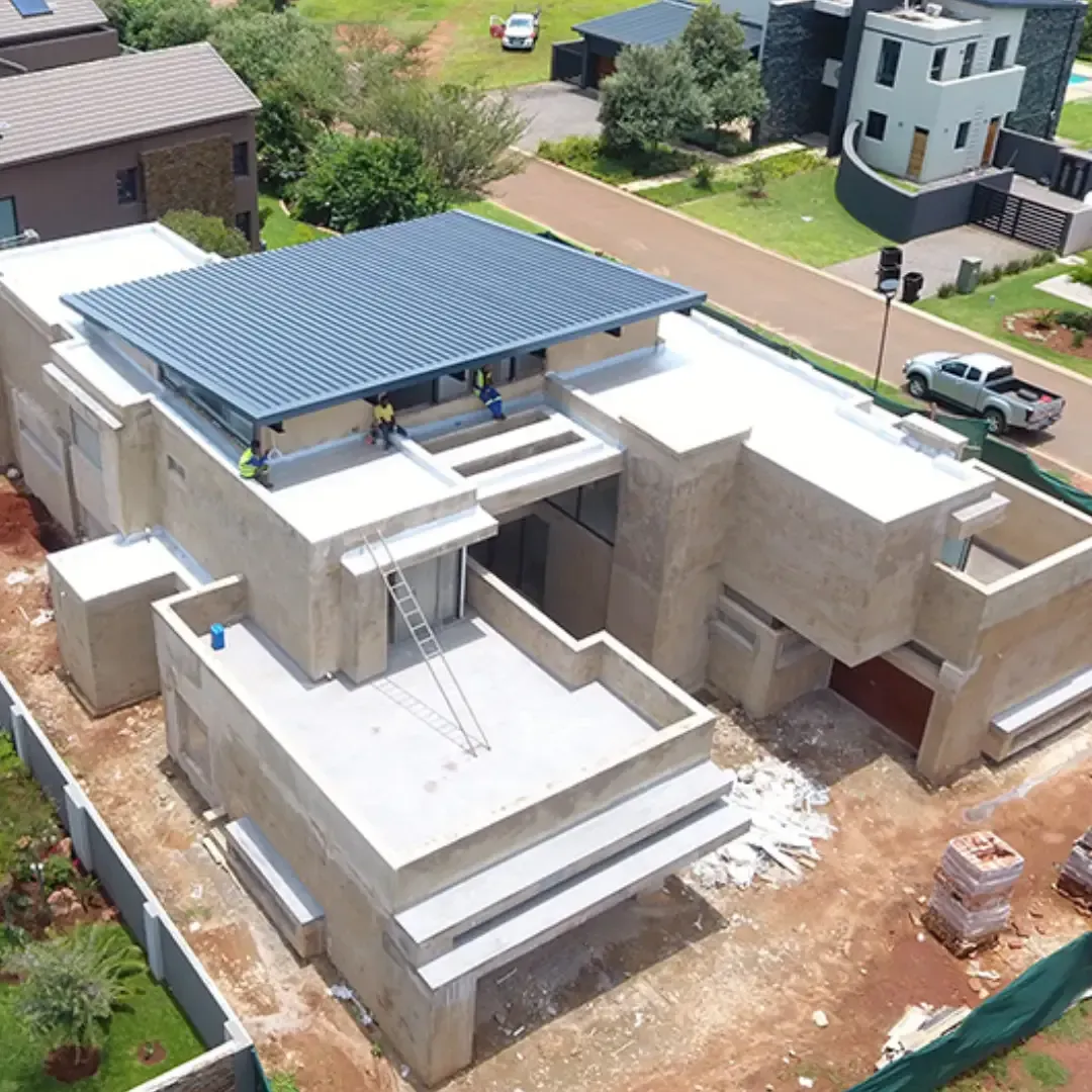 Aerial view of a modern house under construction with a blue metal roof and concrete walls.