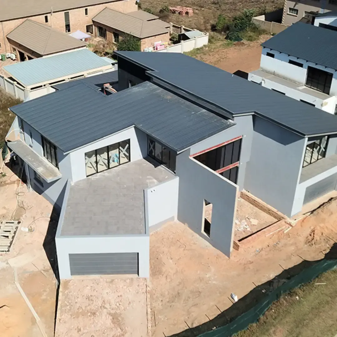 Aerial view of a modern gray house with a dark metal roof and garage on a sandy lot.