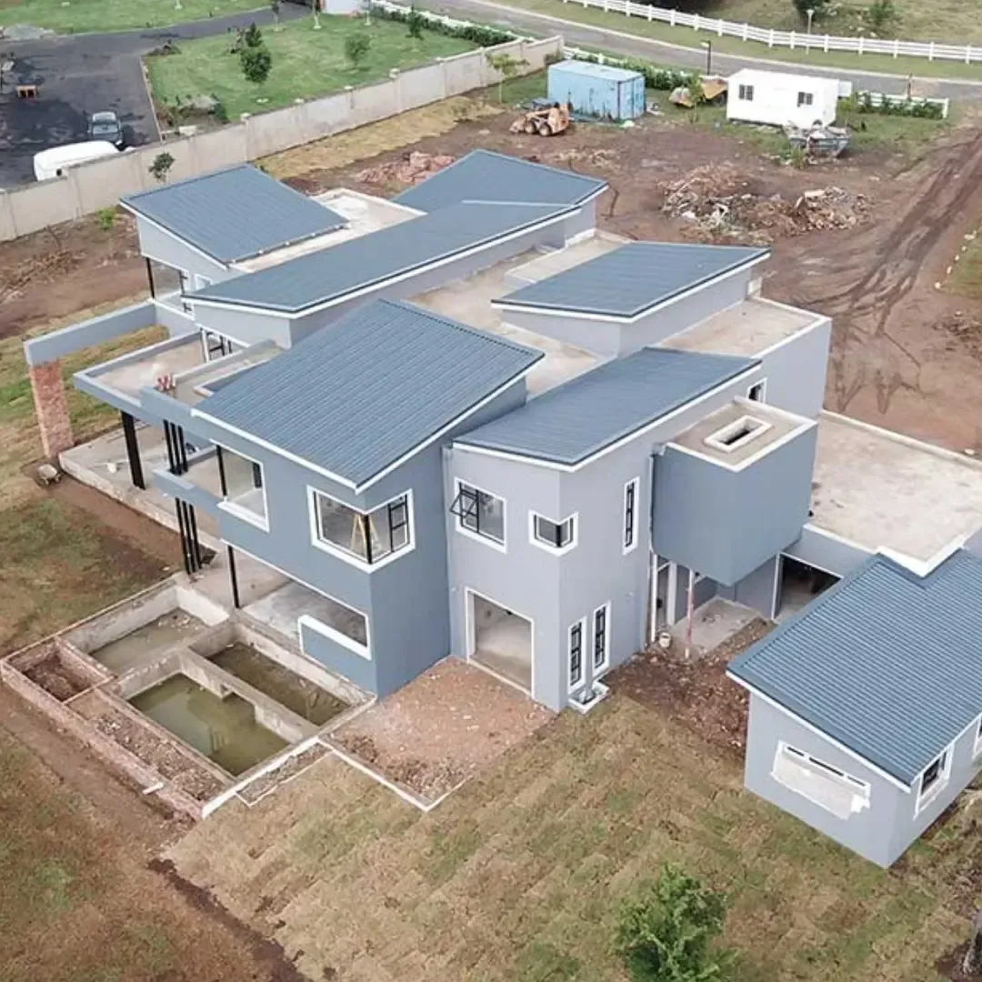 Aerial view of a modern blue-gray house with a metal roof and surrounding dirt yard under construction