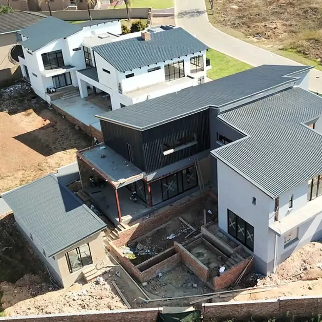 Aerial view of a modern white house with gray roofs and a central black courtyard in a dirt lot under construction