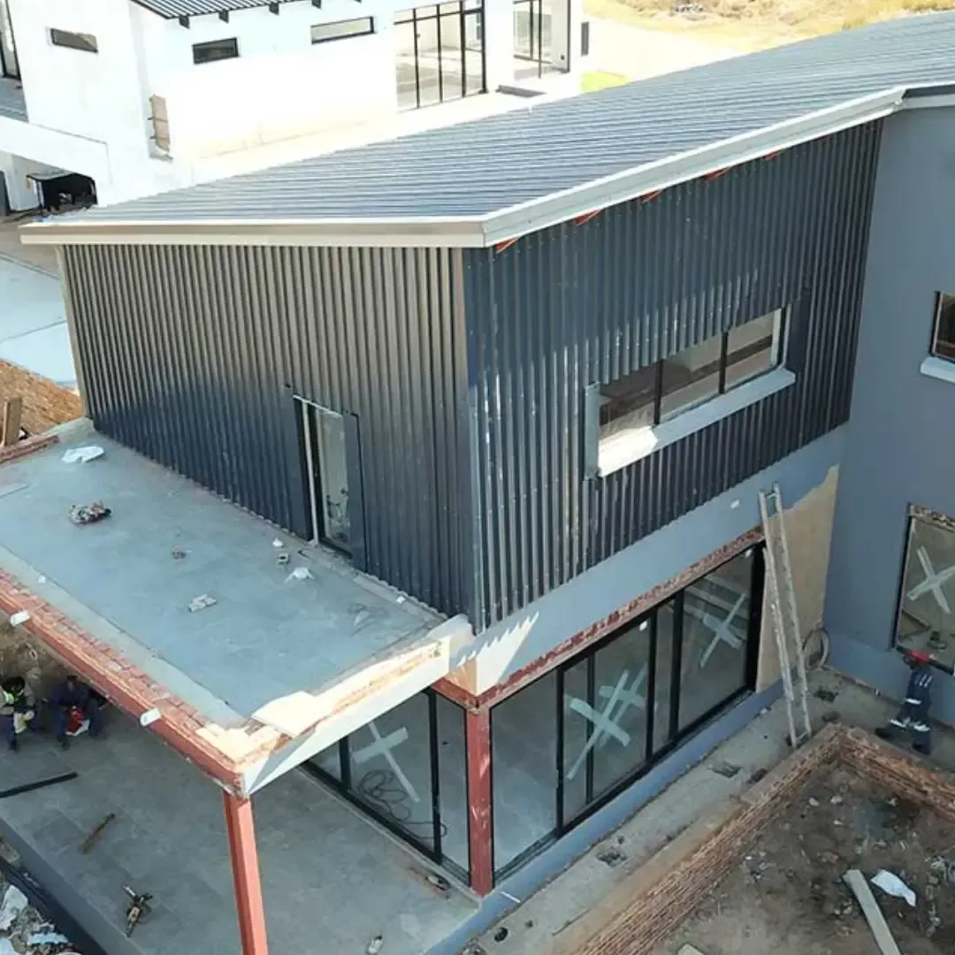 Modern dark-clad building with sloped roof and large windows, viewed from above during construction