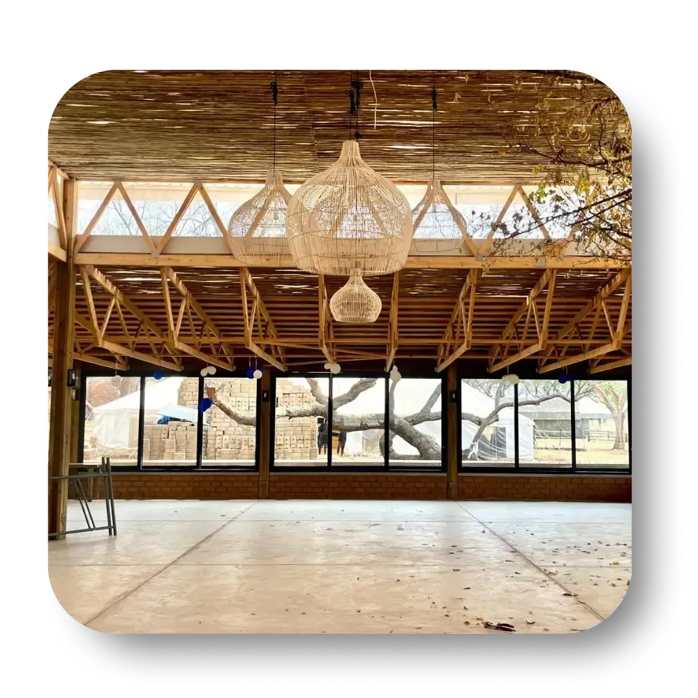 Empty rustic loft with wooden rafters, large windows, and hanging wicker chandeliers.