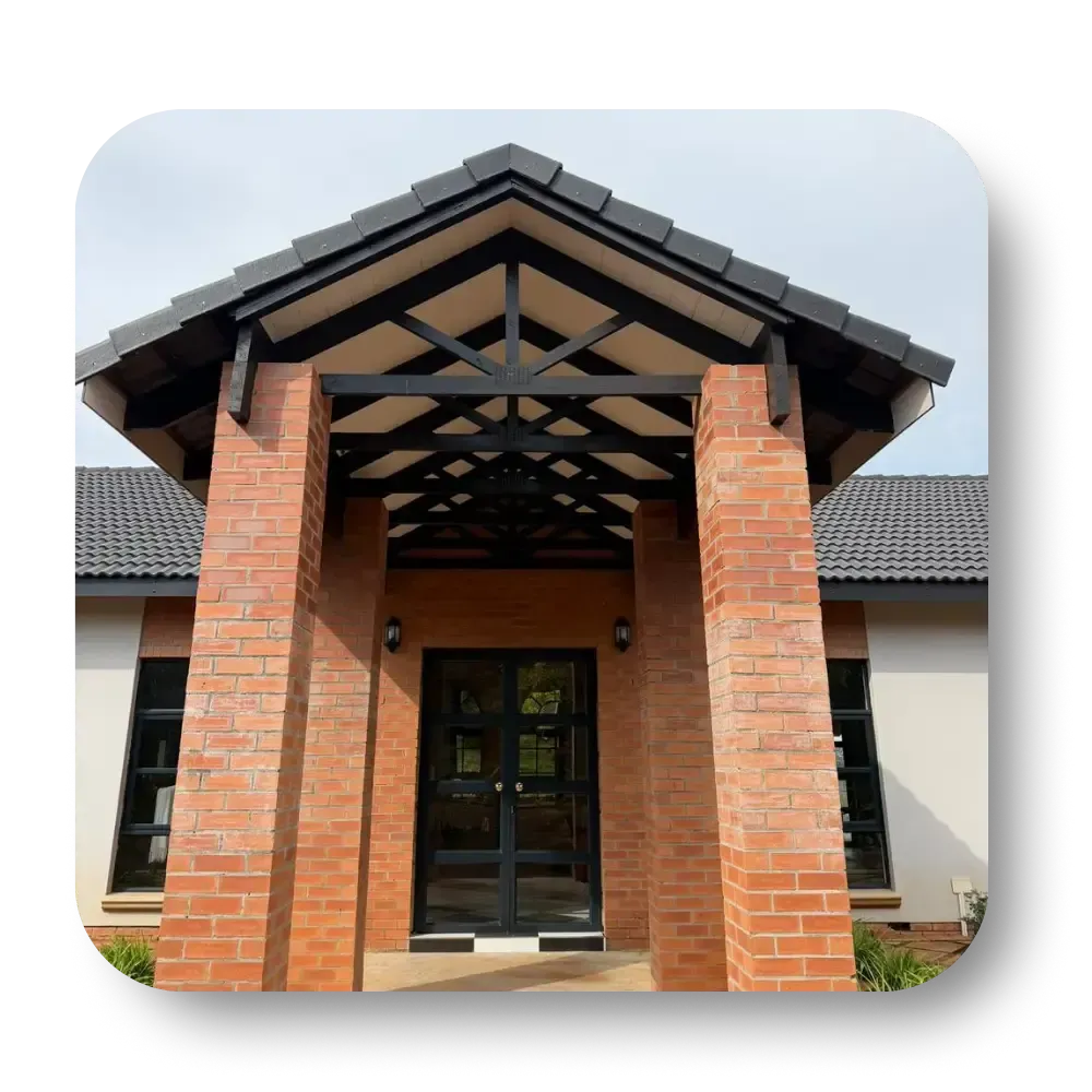 Brick entrance with dark wood double doors and a peaked roof supported by brick pillars