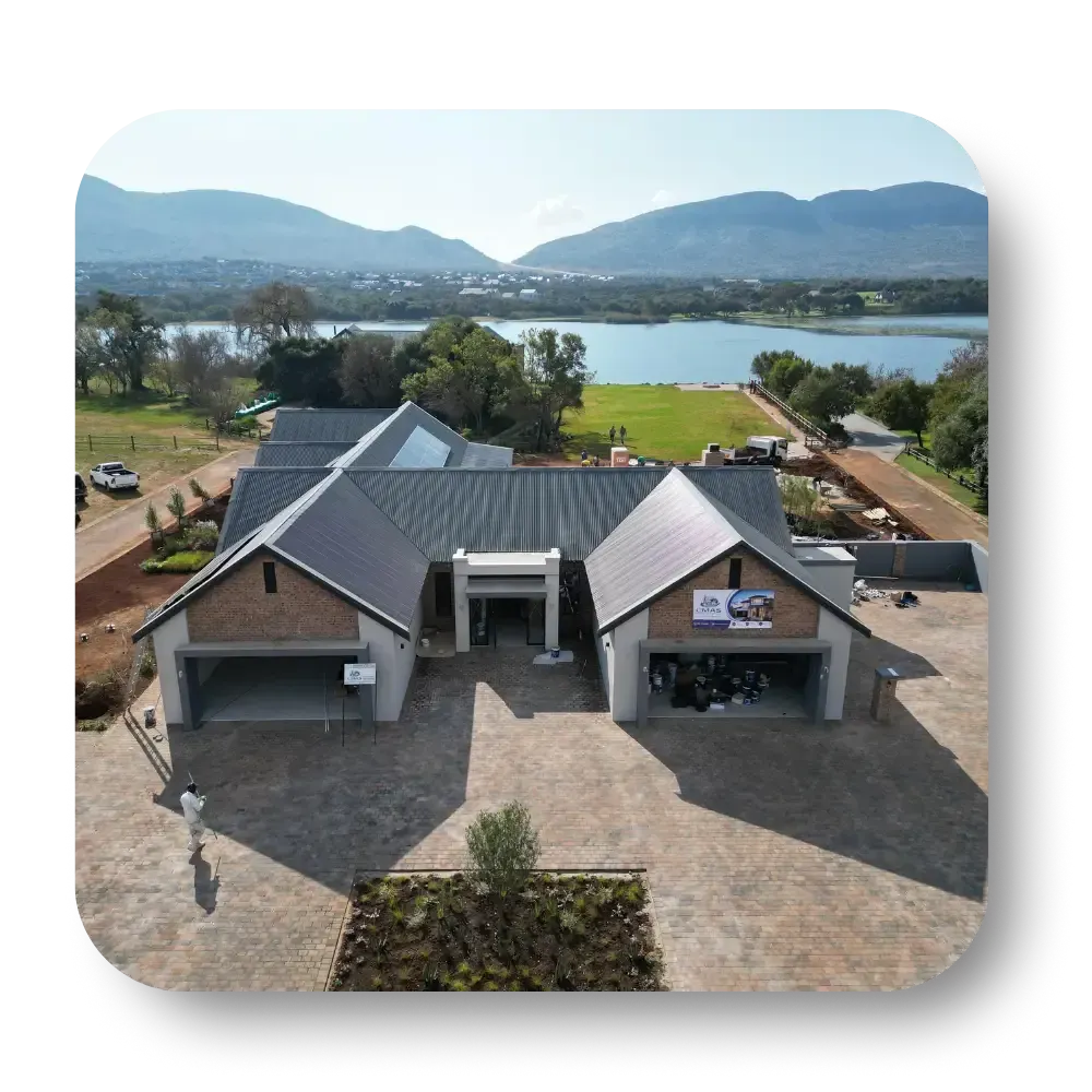 Aerial view of a modern house with a driveway, lake, and mountains in the background