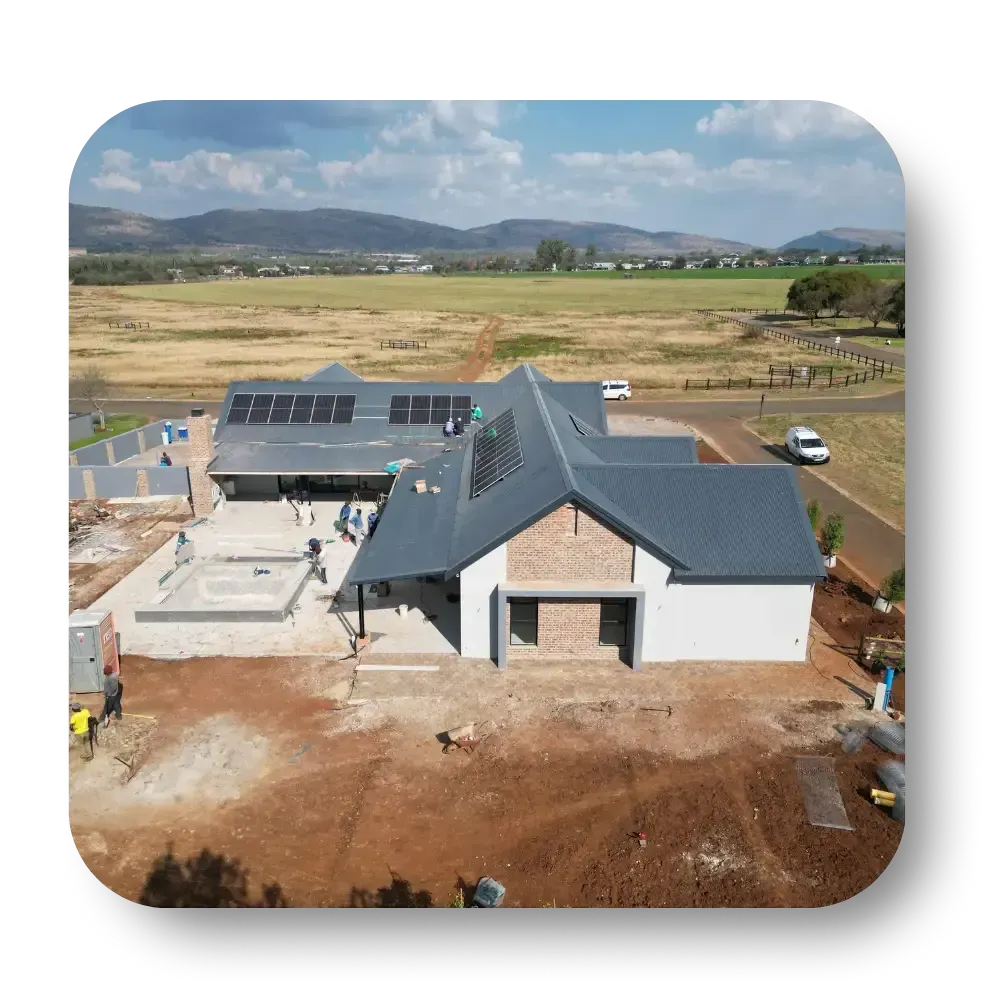 Aerial view of a modern house with a gray roof and solar panels in a rural landscape.