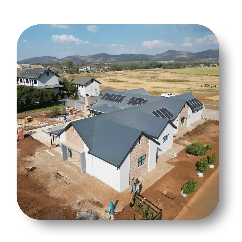 Aerial view of a new house with solar panels in a rural development, surrounded by open land and distant hills
