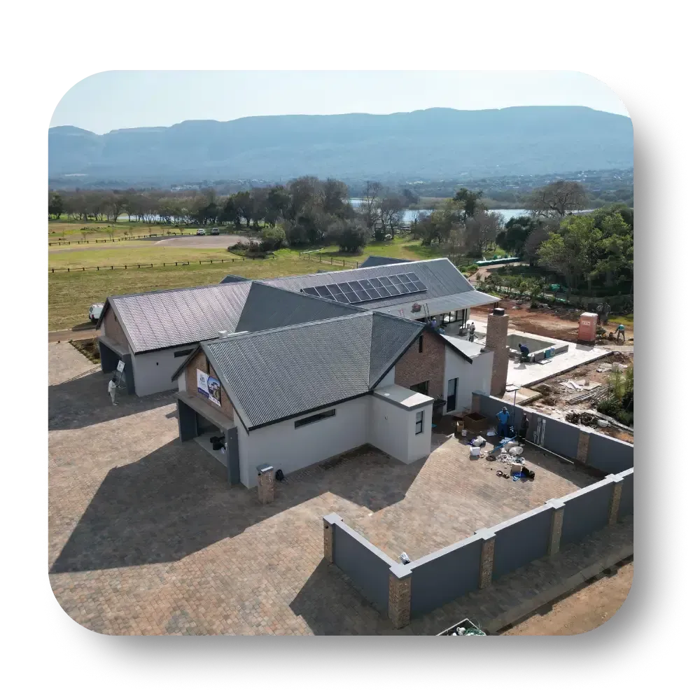 Aerial view of a gray-roofed house with a fenced yard, set against fields and distant mountains.