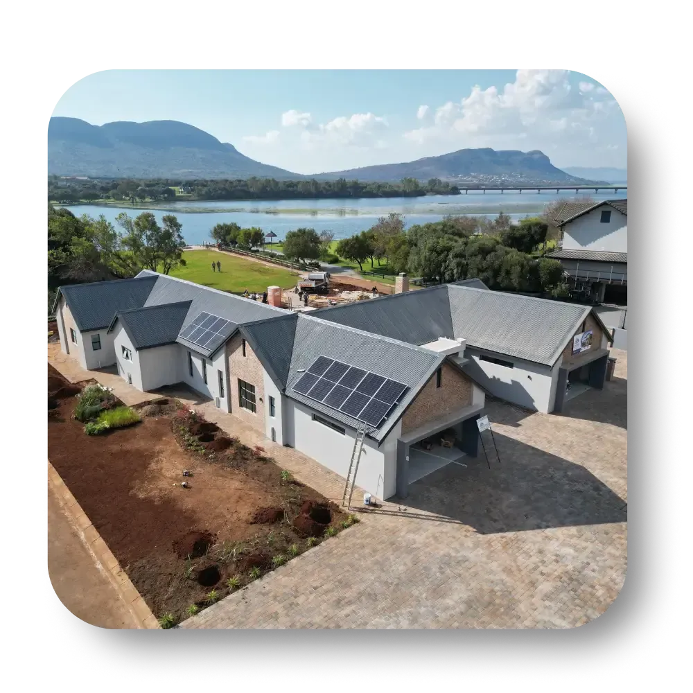Modern gray house with solar panels overlooking a lake and mountains under a partly cloudy sky