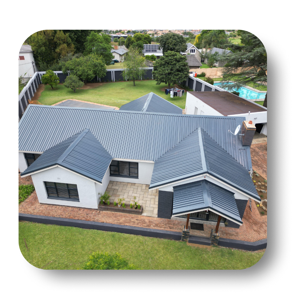 Aerial view of a modern house with a gray metal roof, brick walls, and a green yard.