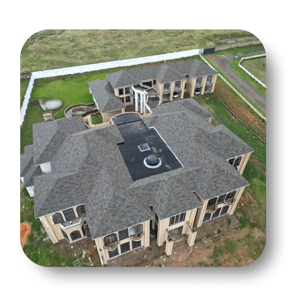 Aerial view of a large gray-roofed house with a central courtyard and surrounding green lawn.