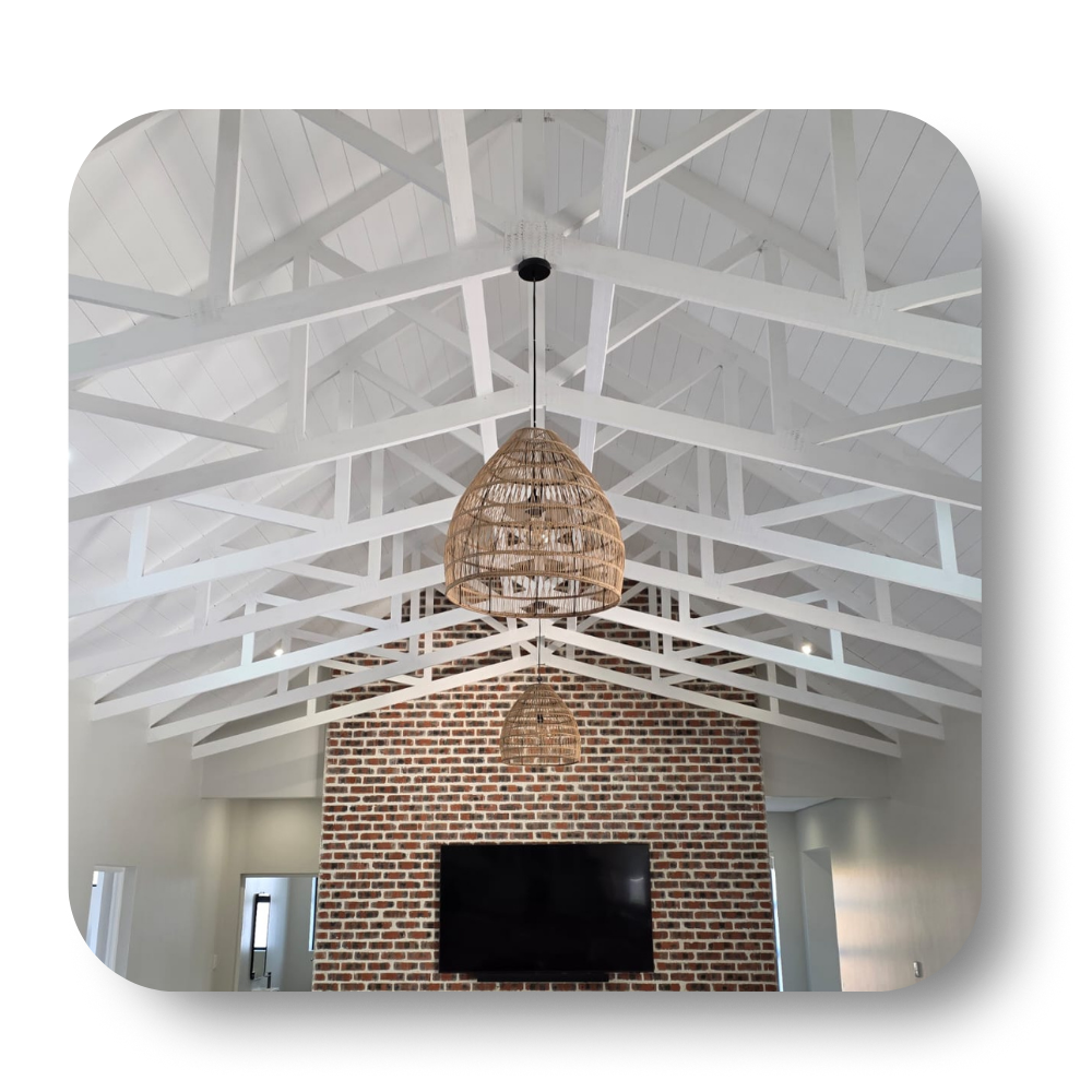White vaulted ceiling with exposed beams, woven pendant light, and brick wall above a wall-mounted TV
