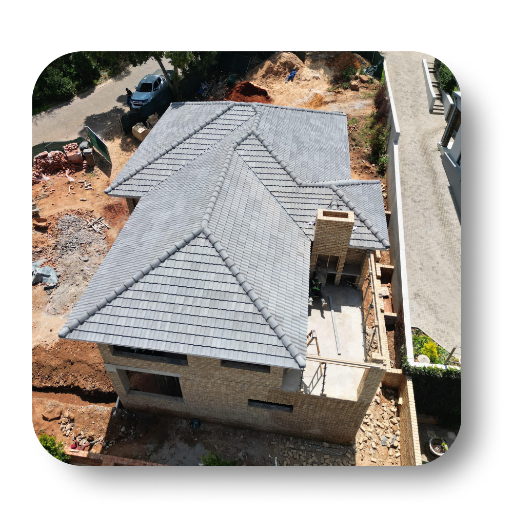 Aerial view of a house with a gray shingle roof and brick exterior beside a driveway and construction dirt.