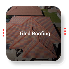 Tiled roofing on a house, aerial view. Multi-colored tiles, red trim, green lawn in background.