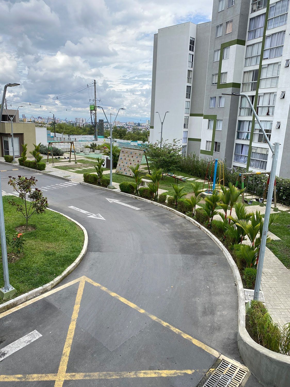 Sendero curvo pavimentado en un complejo de apartamentos ajardinado junto a edificios altos bajo un cielo nublado.