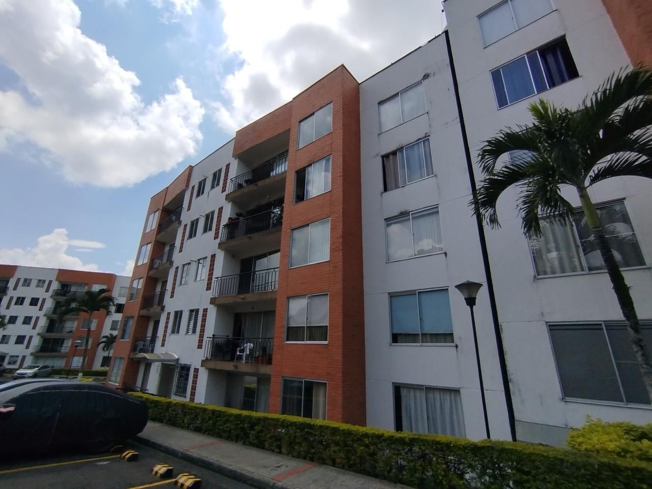 Edificios de apartamentos modernos con balcones y palmeras bajo un cielo nublado.