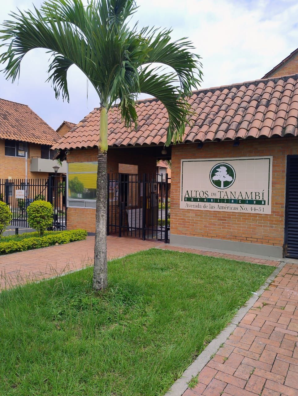 Entrada a Atos Pharma con techo de tejas, palmera y un pequeño patio con césped.