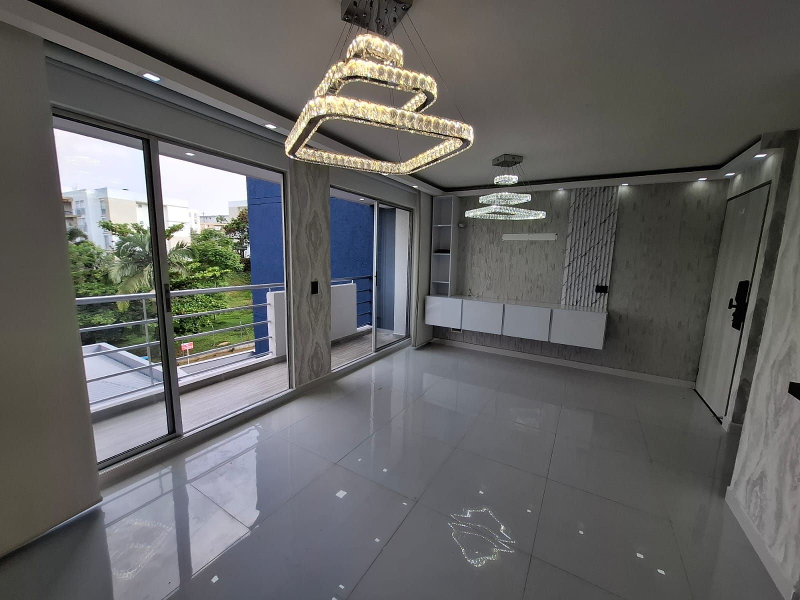 Sala de estar moderna y vacía con suelo de baldosas brillantes, grandes ventanales, vistas al balcón y luces en el techo.