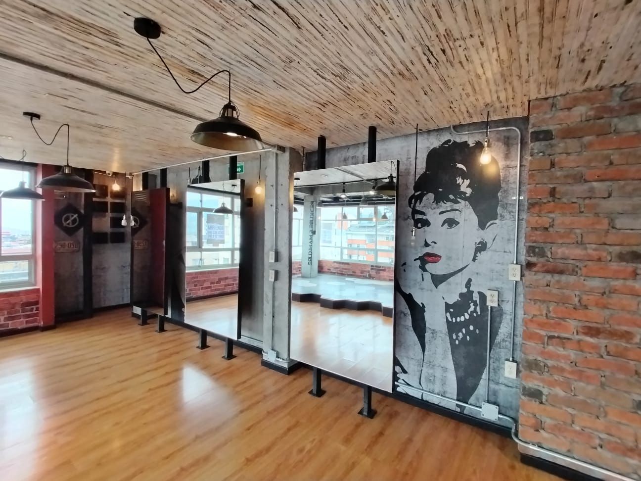 Interior tipo loft con paredes de ladrillo, suelo de madera, lámparas colgantes y un gran mural en blanco y negro.